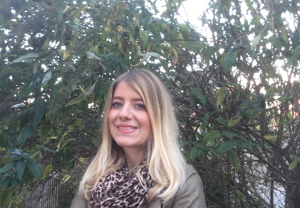Jude, FADT Engagement Worker, Chester & Liverpool. Portrait photo of a women smiling, standing in front of foliage.