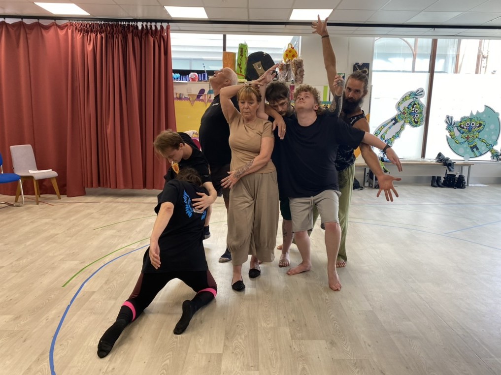 A group of dancers connected with movements on different levels in the middle of a rehearsal room